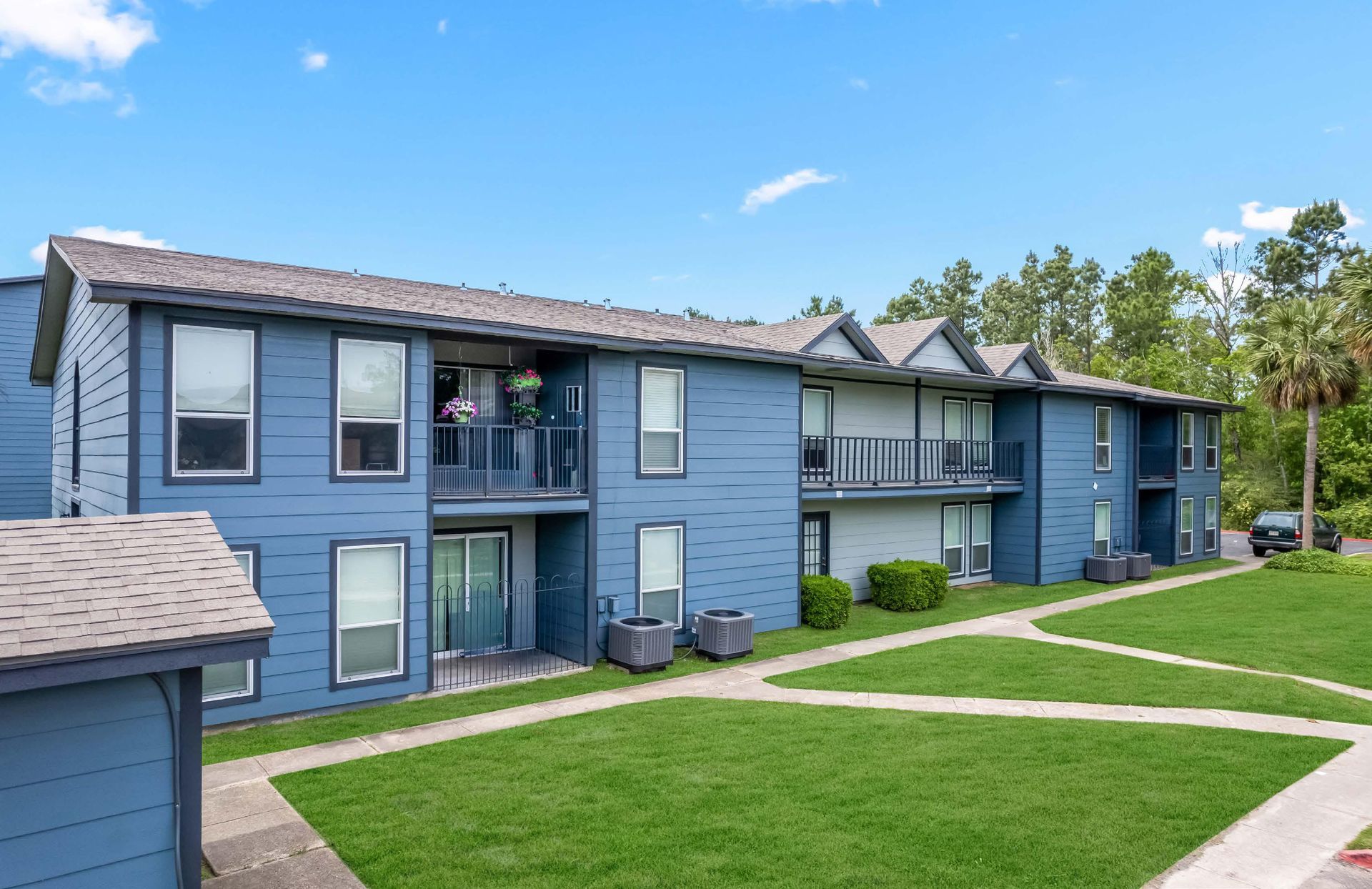 Blue apartment buildings with balconies and green lawns under a clear sky