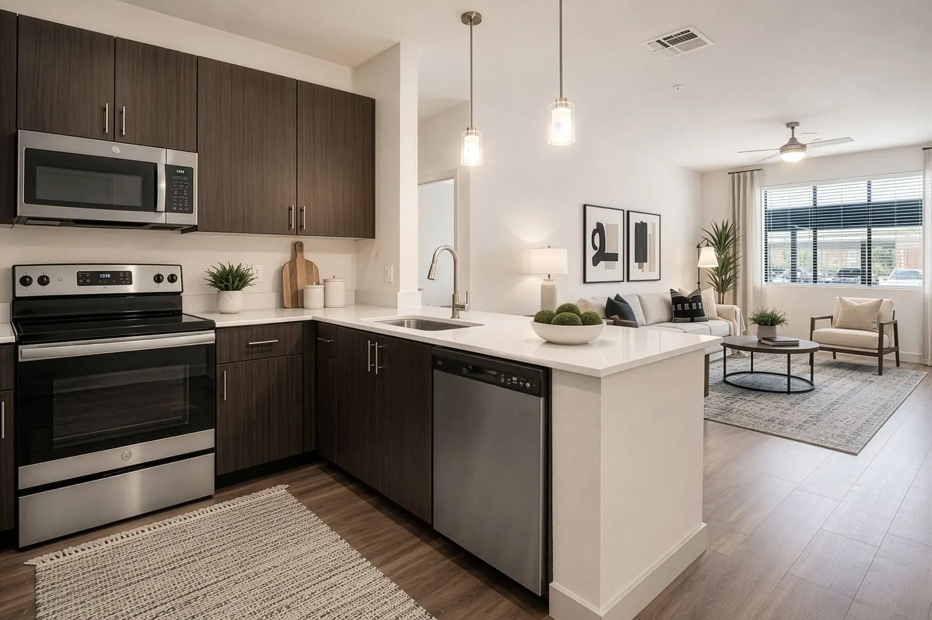 Modern kitchen with dark wood cabinets, stainless steel appliances, and white countertops opening into a living area.