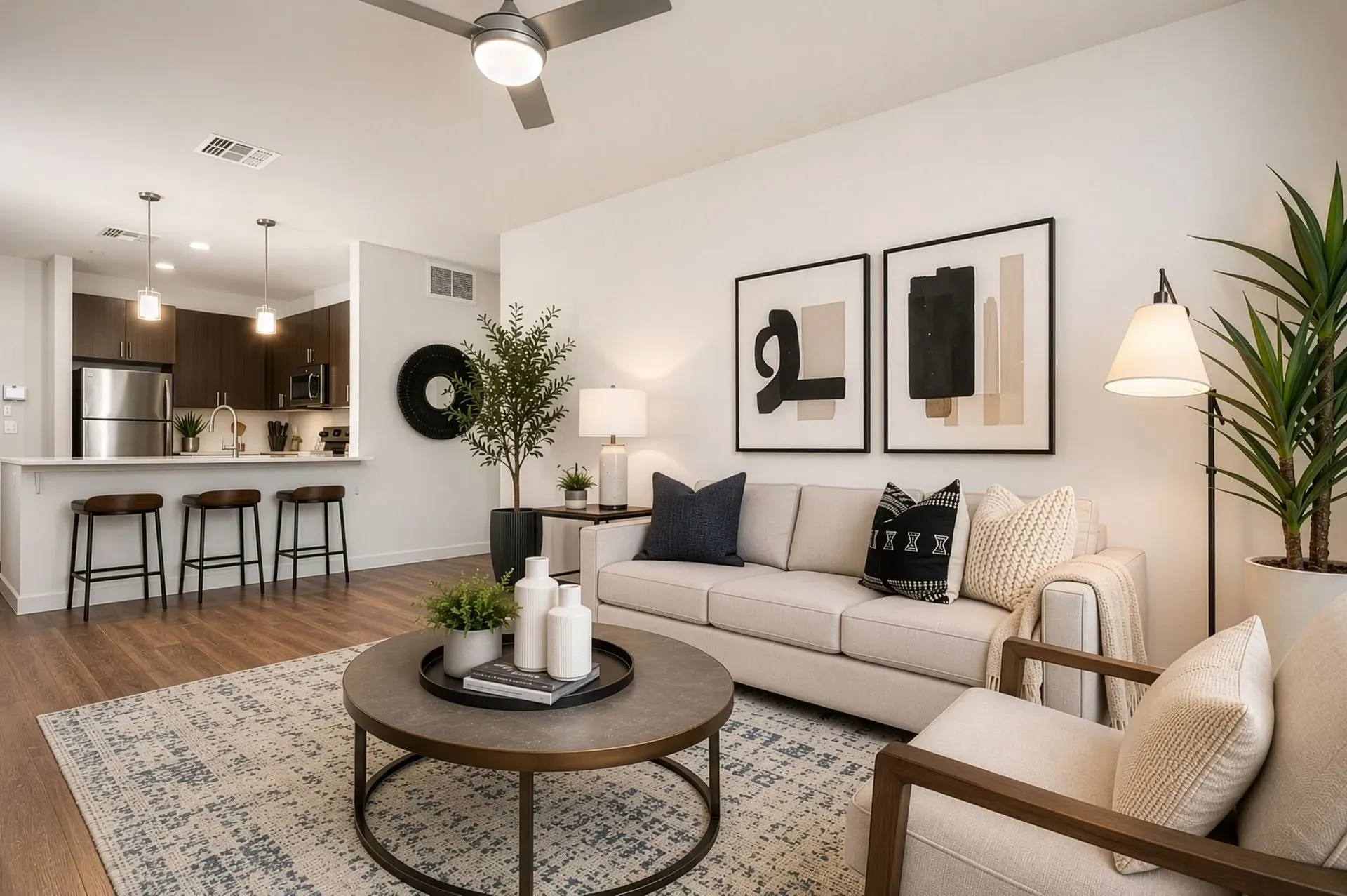 A modern living room with a sofa, armchair, coffee table, and a view of the kitchen with bar stools.