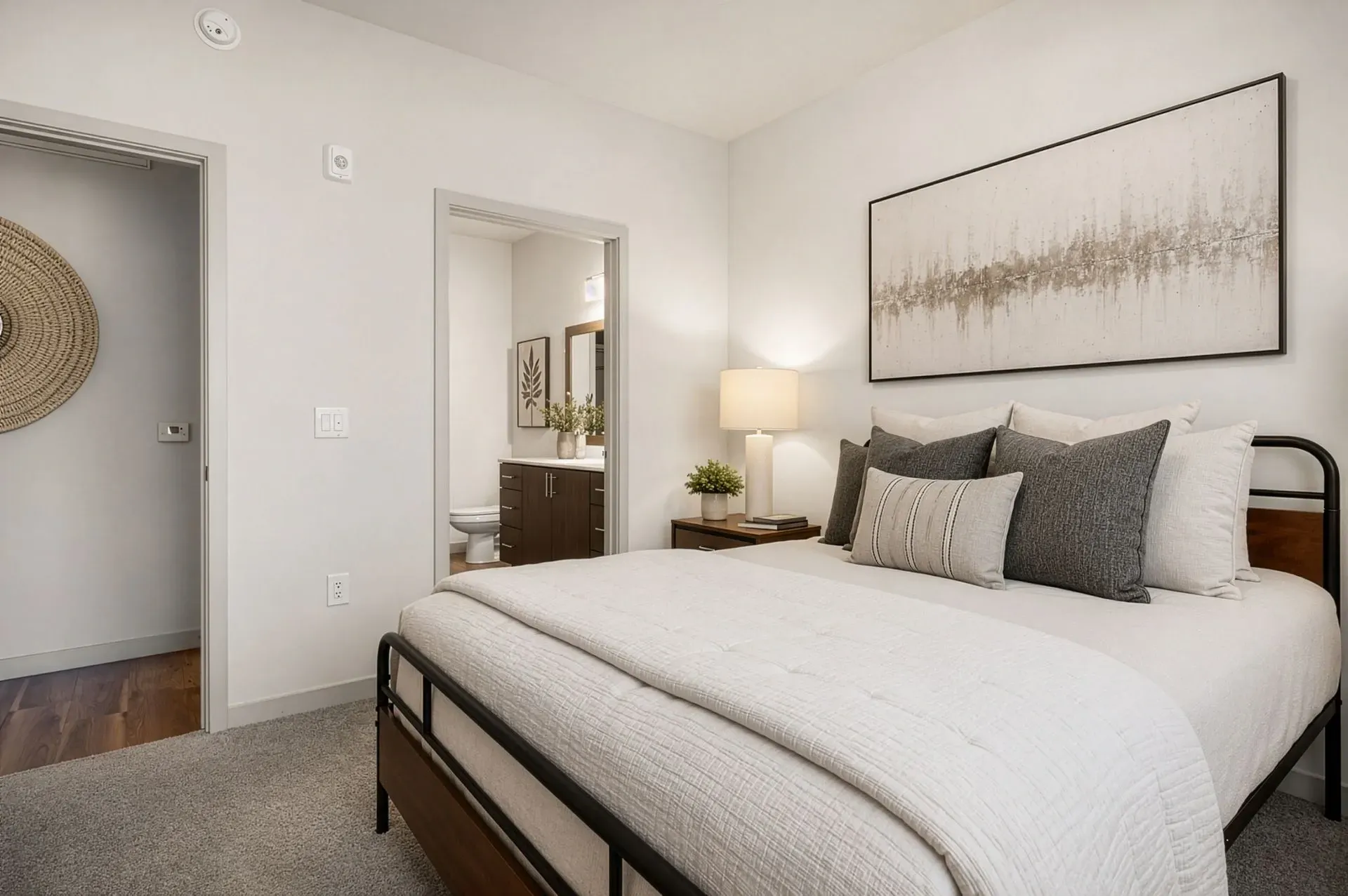 Cozy bedroom with a large bed, nightstand, and an ensuite bathroom visible through an open doorway at Parc Lofts in Tolleson, AZ.