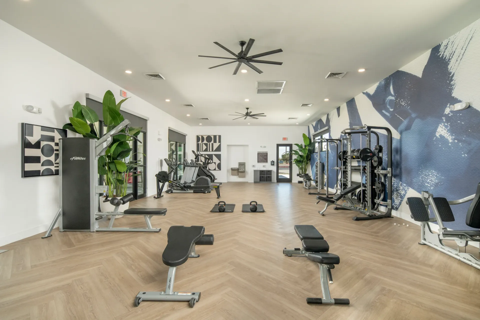 Modern gym with cardio machines, weight machines, benches, and kettlebells at Parc Lofts in Tolleson, AZ.