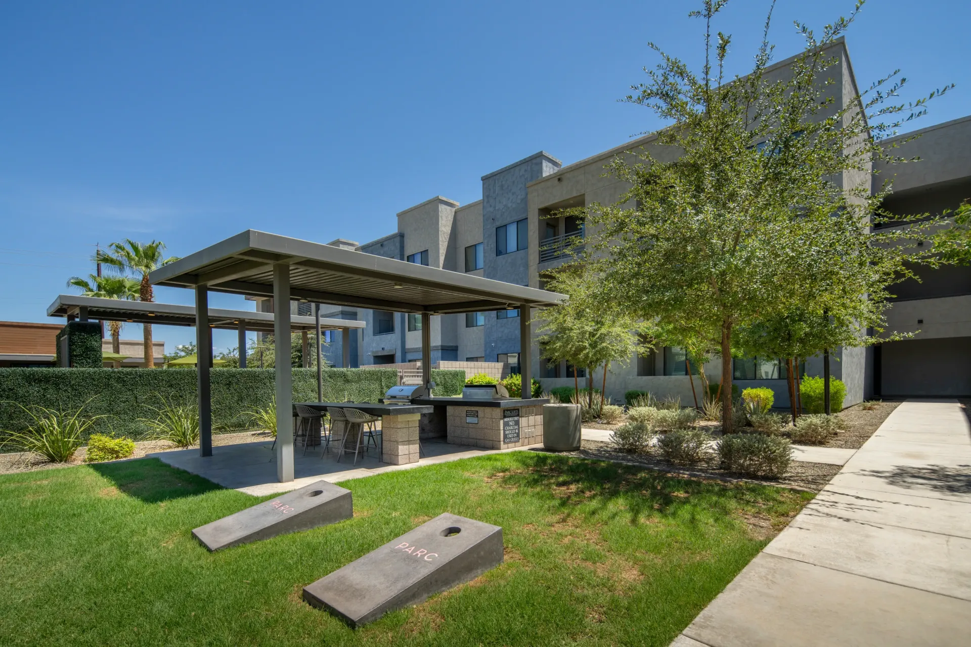 Outdoor barbecue area with grills, seating, and cornhole boards at Parc Lofts in Tolleson, AZ.