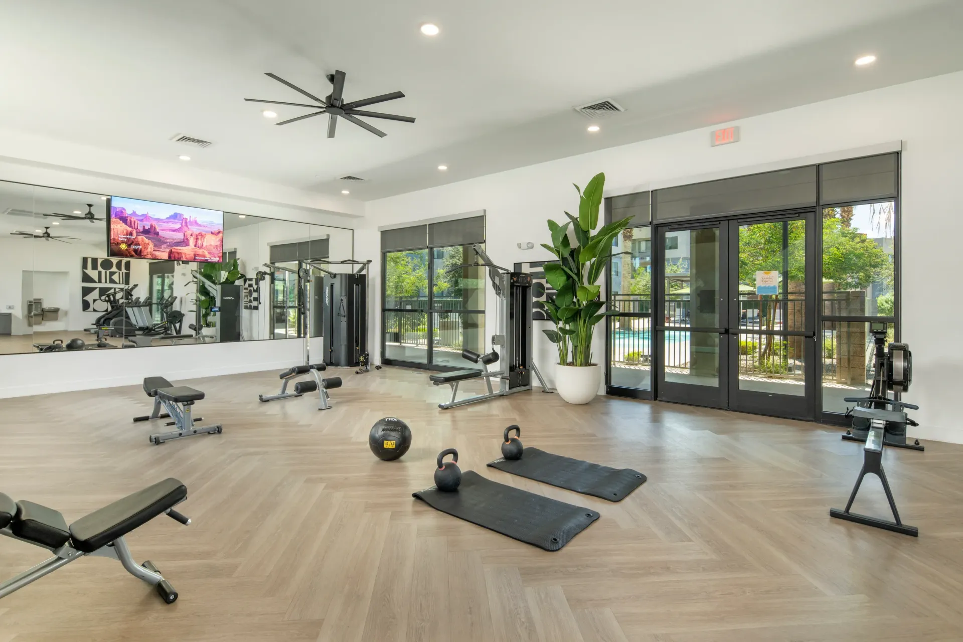 Modern apartment fitness center with cardio machines, free weights, yoga mats, and view of the pool at Parc Lofts in Tolleson, AZ.