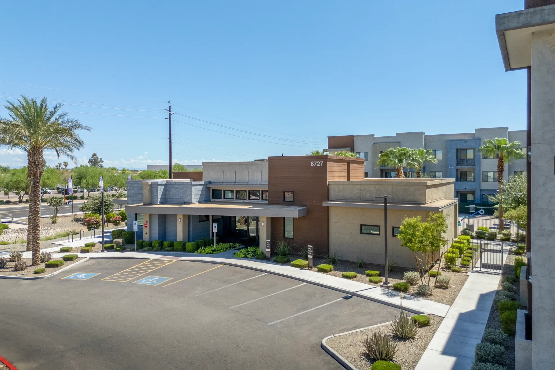 Exterior view of apartment building entrance with parking lot and palm treesat Parc Lofts in Tolleson, AZ.