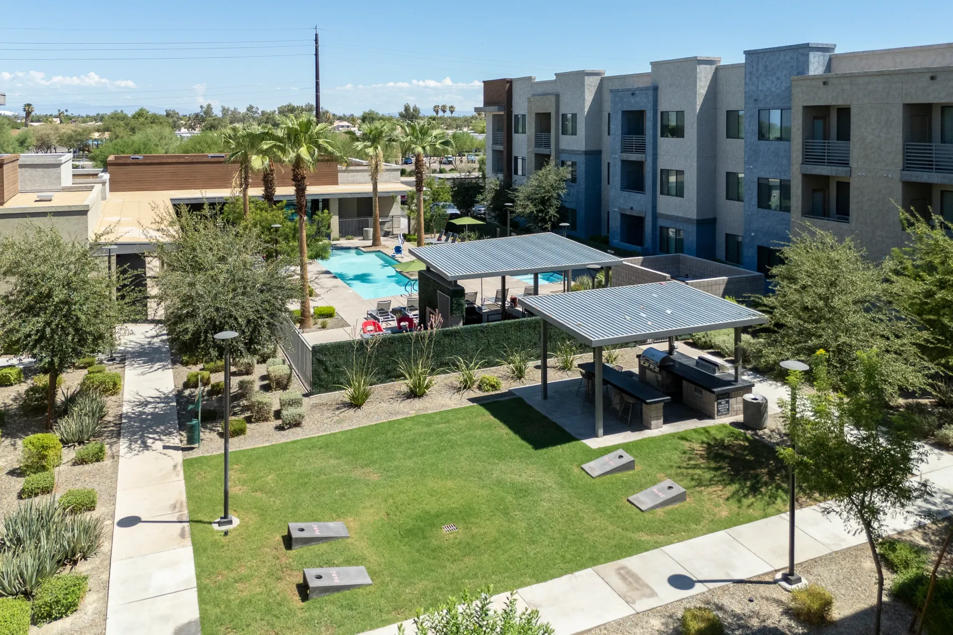 Outdoor community area with a swimming pool, grilling stations, and cornhole game.