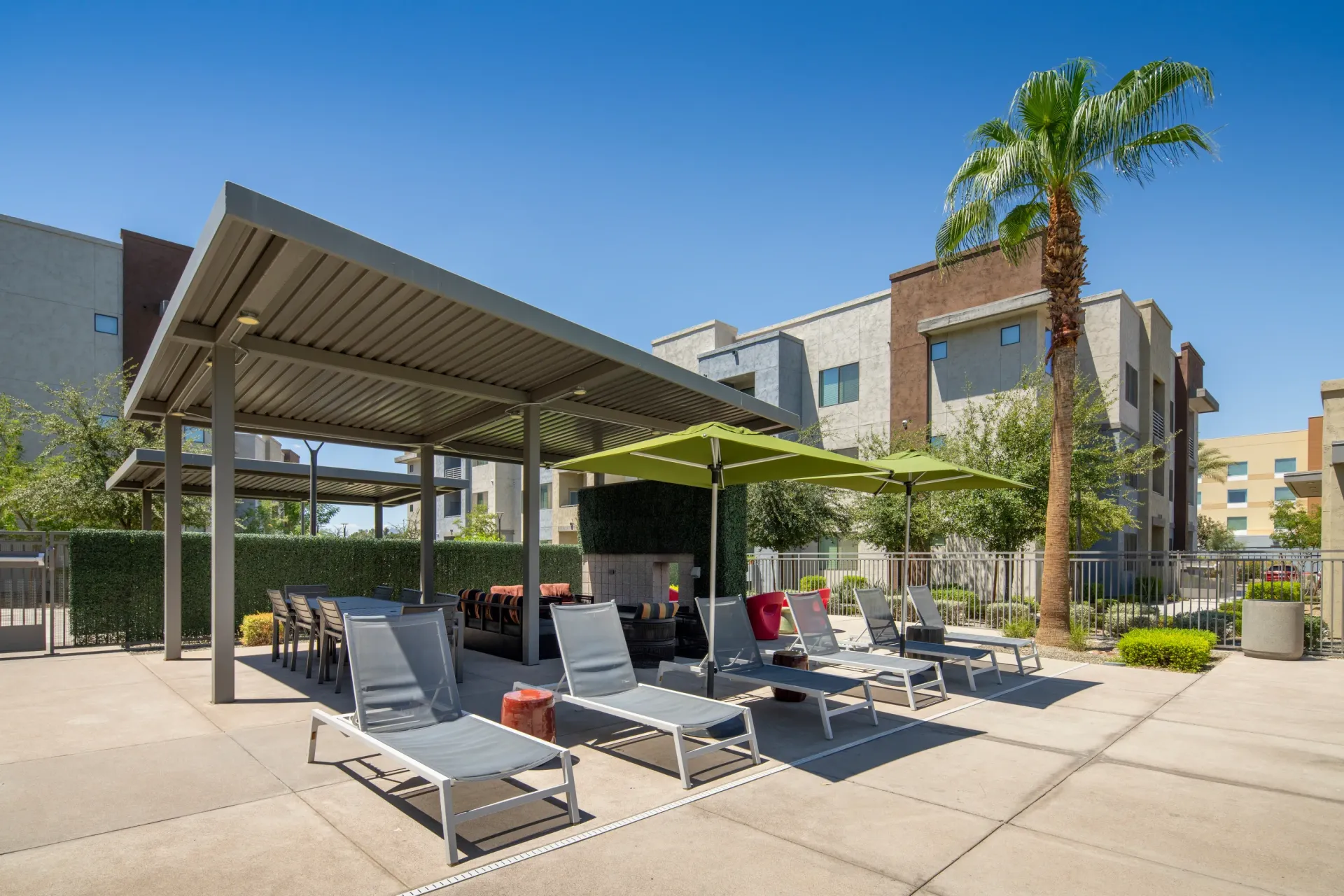 Outdoor lounge area with covered seating, chaise lounges, and a fireplace under a palm tree at Parc Lofts in Tolleson, AZ.
