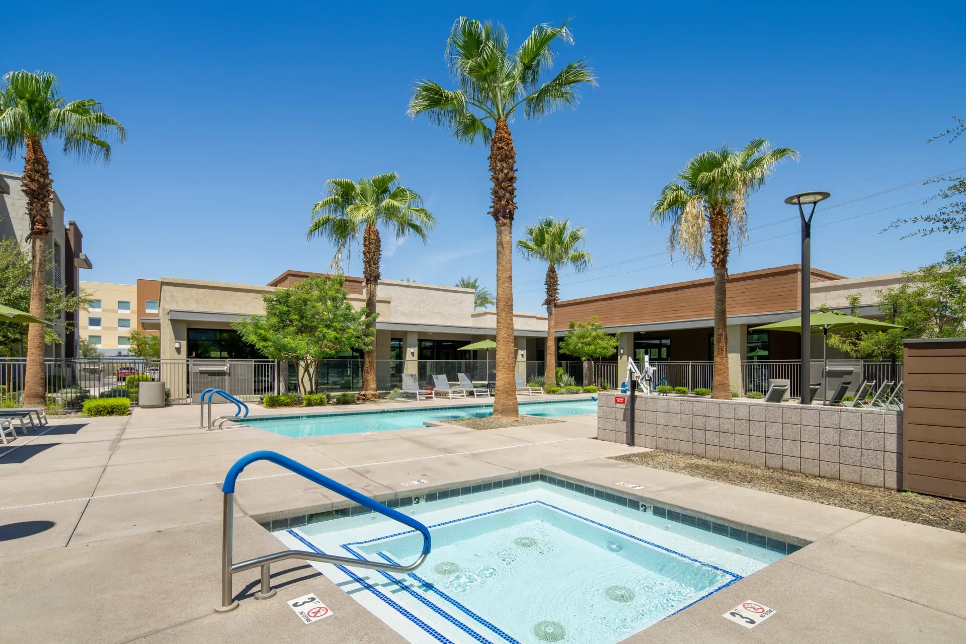 Swimming pool and hot tub area with palm trees and lounge chairs at Parc Lofts in Tolleson, AZ.