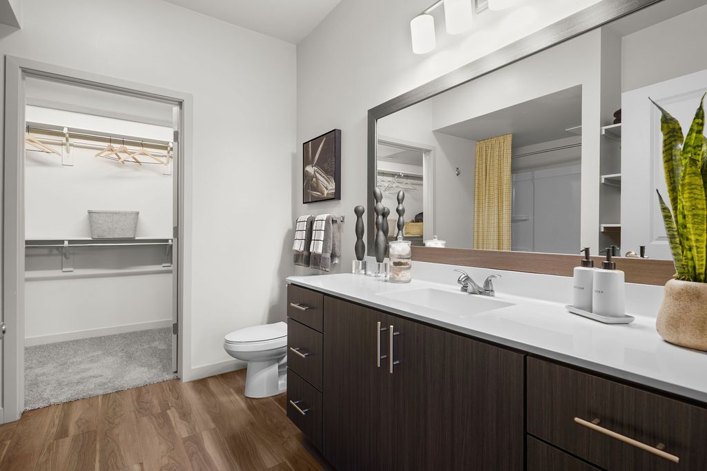 Parc Lofts Bathroom with double-sink vanity, large mirror, and walk-in closet visible through an open doorway.