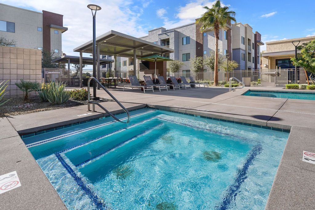 Parc Lofts  pool area with a metal handrail, lounge chairs, shaded seating, and surrounding apartment buildings.