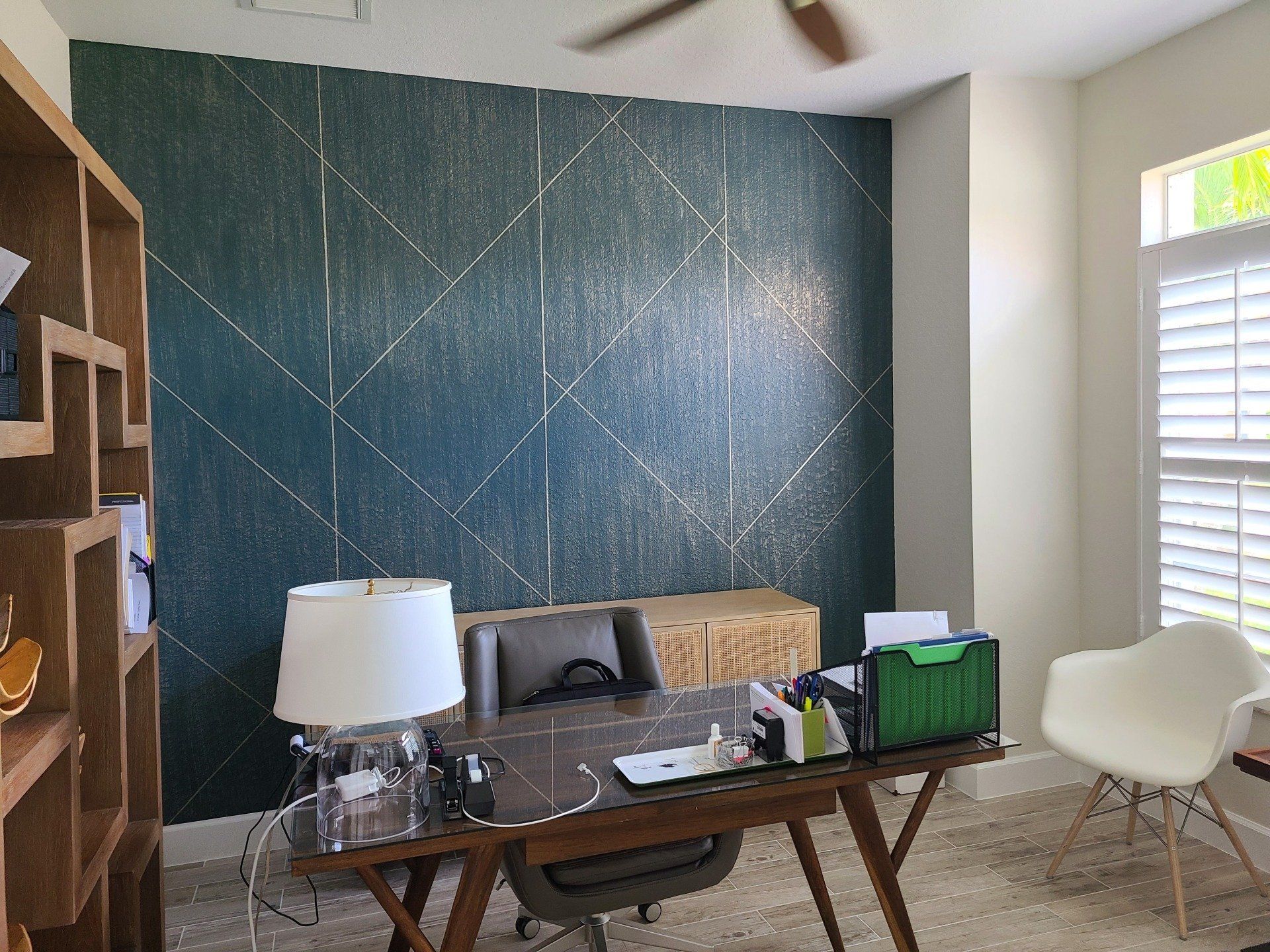 Home office with teal geometric accent wall, desk, chair, and bookshelf.