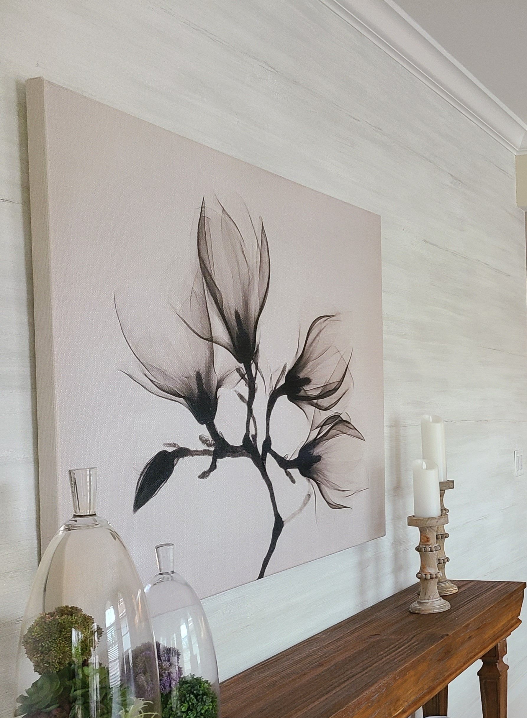 Painting of black magnolia flowers on a wall above a wooden console with decorative candles and glass cloches.