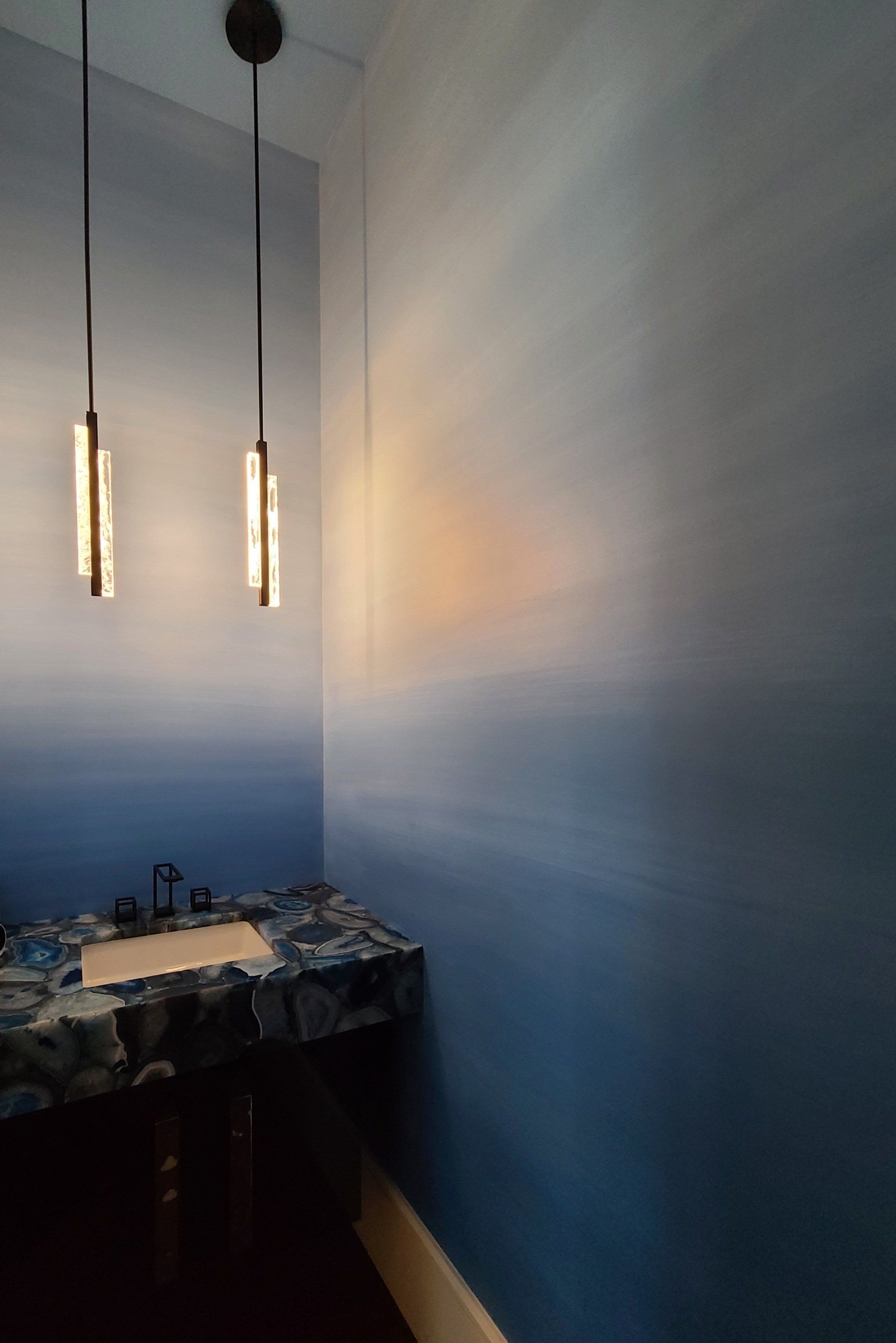 Small blue ombre painted bathroom with hanging lights and a unique stone sink.