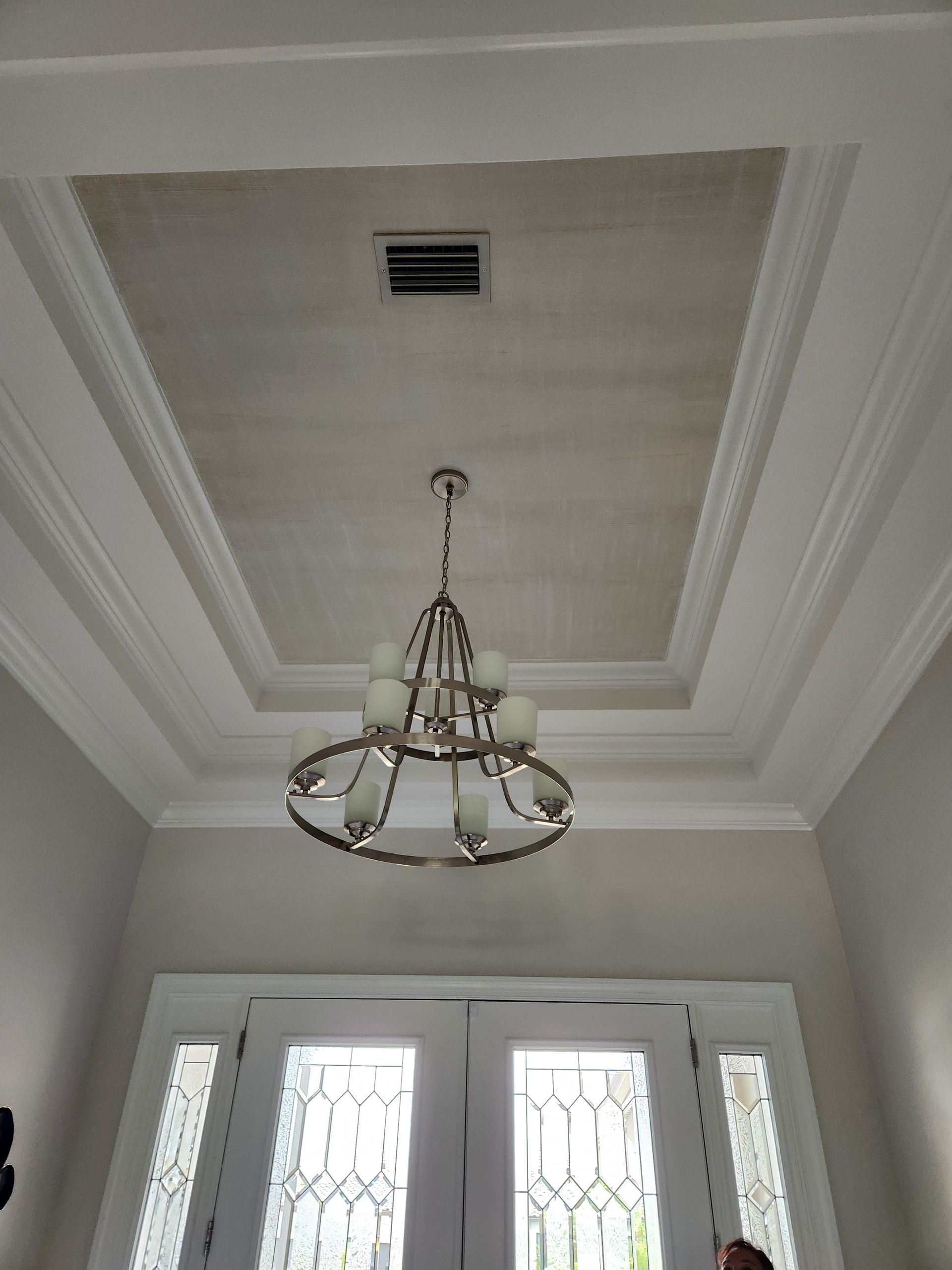 Chandelier hangs from a rectangular ceiling detail above a double door, white trim, and light beige walls.