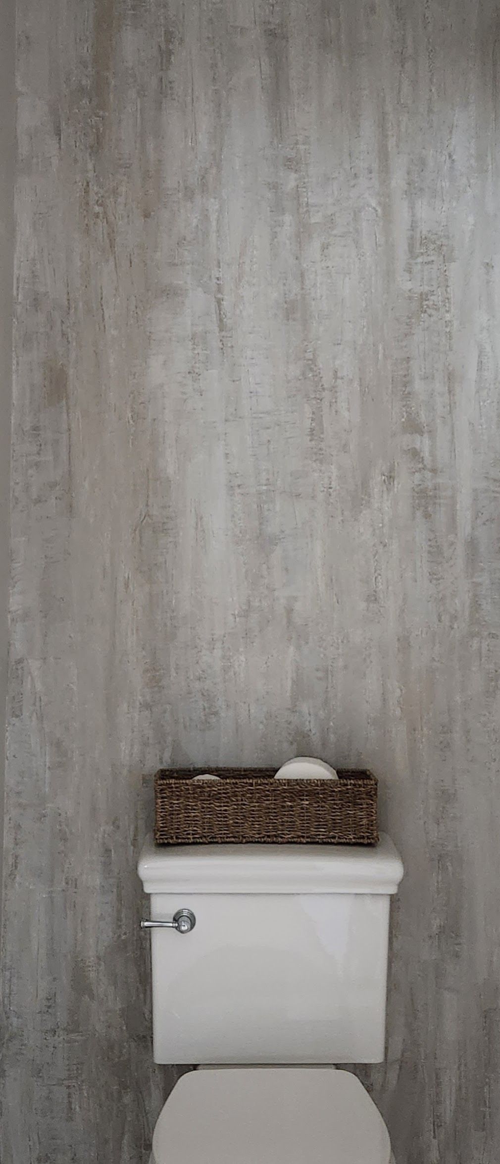 A white toilet with a woven basket on top against a textured gray wall.