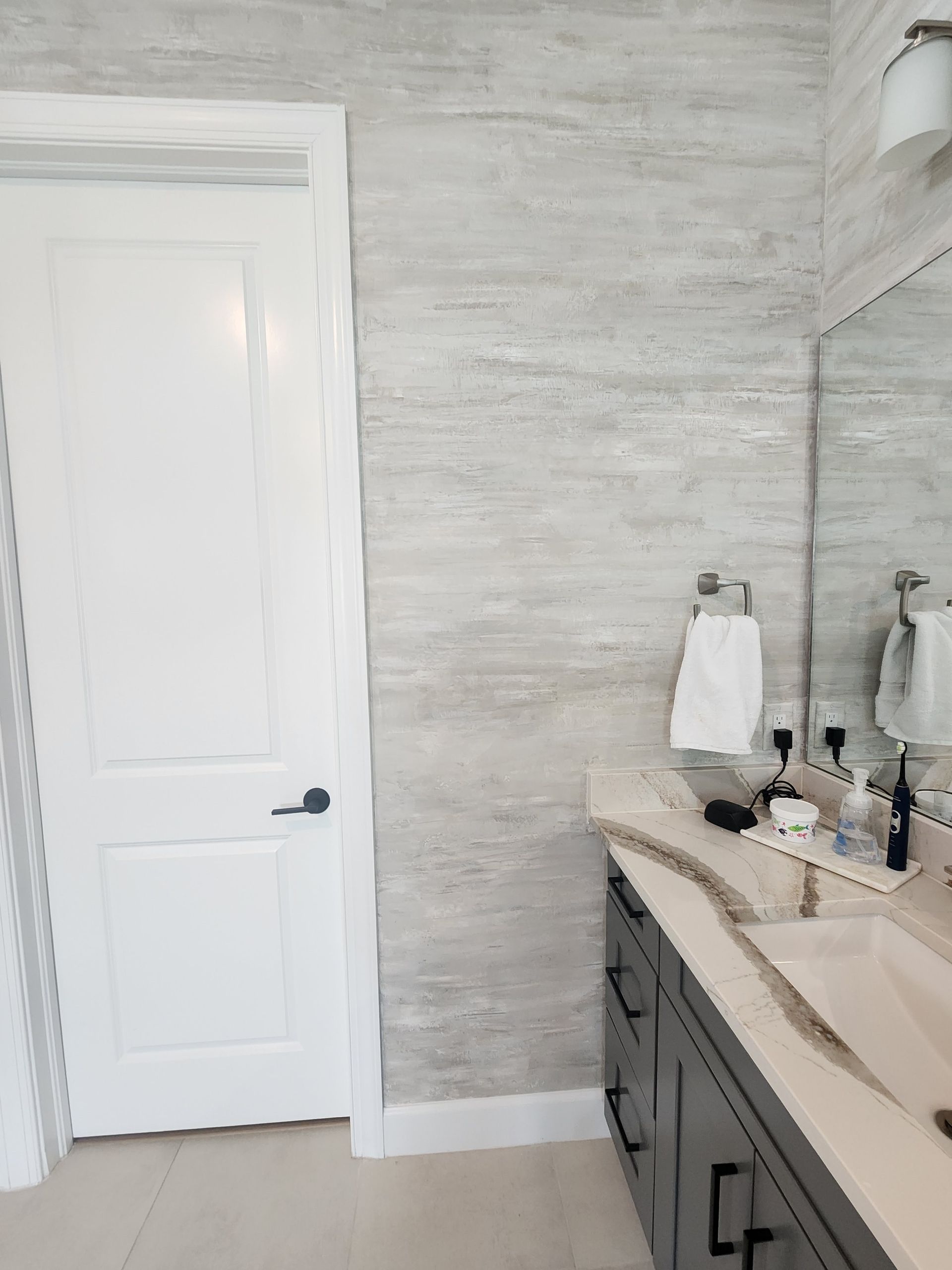 Bathroom with white door, marble-look wall, dark vanity, mirror, and white towel.