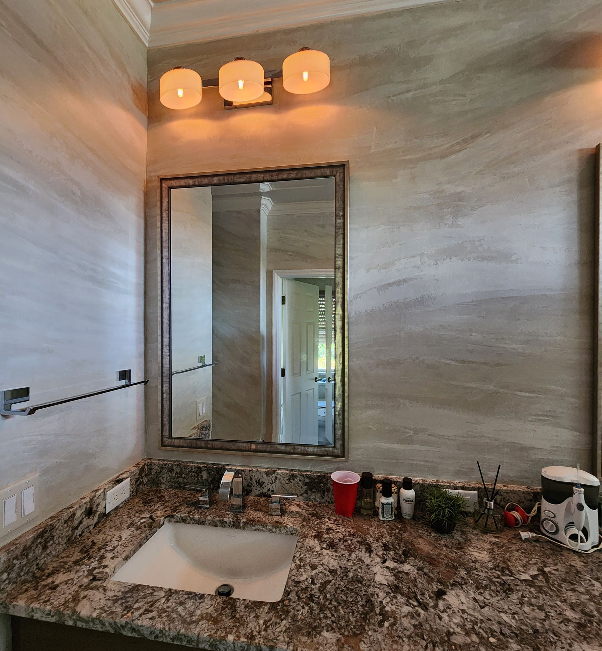 Bathroom with vanity, mirror, and three-light fixture. Granite countertop, neutral wall paint, and sink.