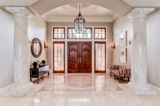 Grand foyer with marble floors, columns, and double wooden doors.