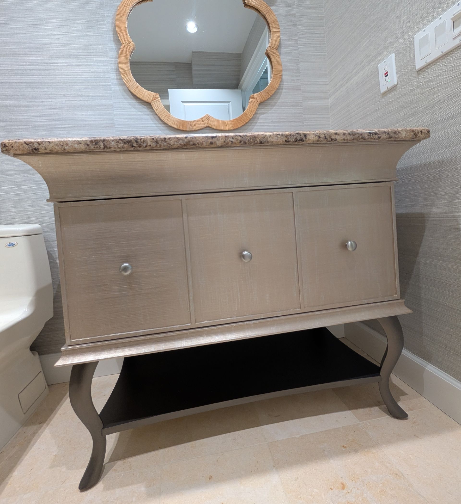 Silver vanity cabinet with a black shelf, decorative mirror, and light-colored walls.