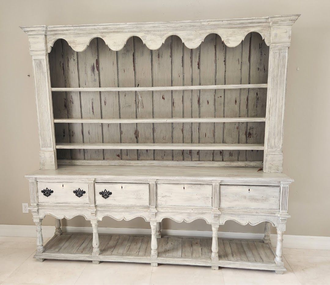 White-painted wooden hutch with shelves, drawers, and decorative scalloped trim; set against a neutral wall.
