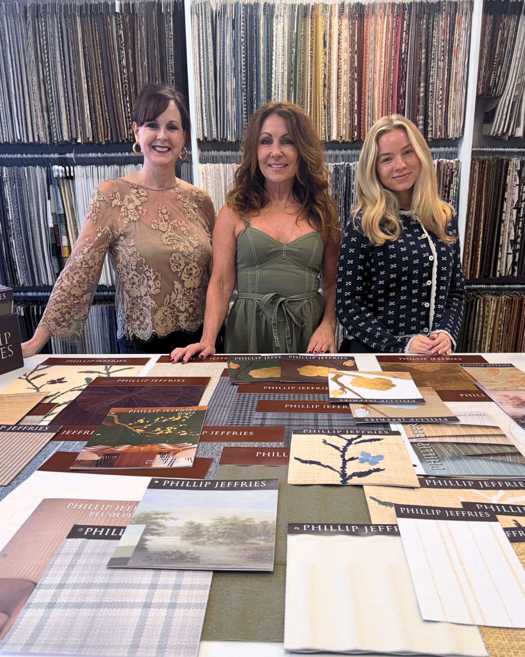 Three interior designers stand behind a table displaying fabric swatches in a showroom.
