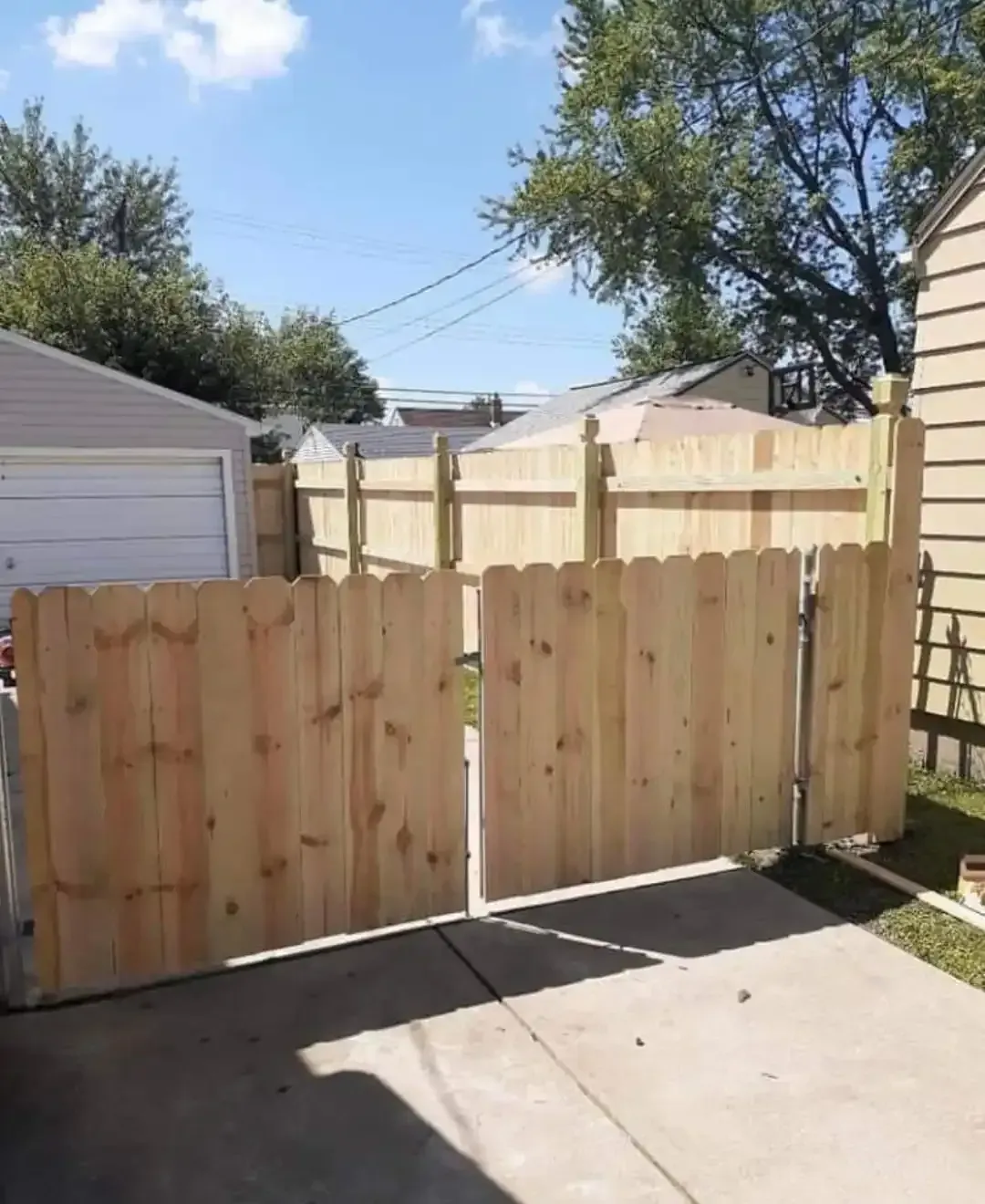 Wooden backyard fence with two gates beside a concrete driveway, under a sunny sky