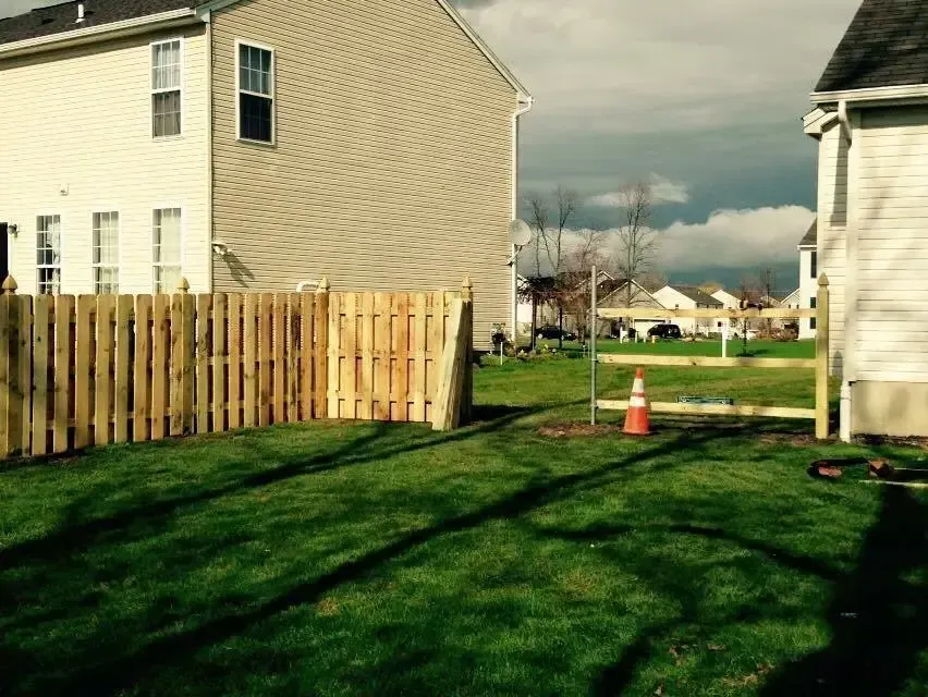 Backyard between beige houses with wooden fence, green grass, and an orange traffic cone near a gate