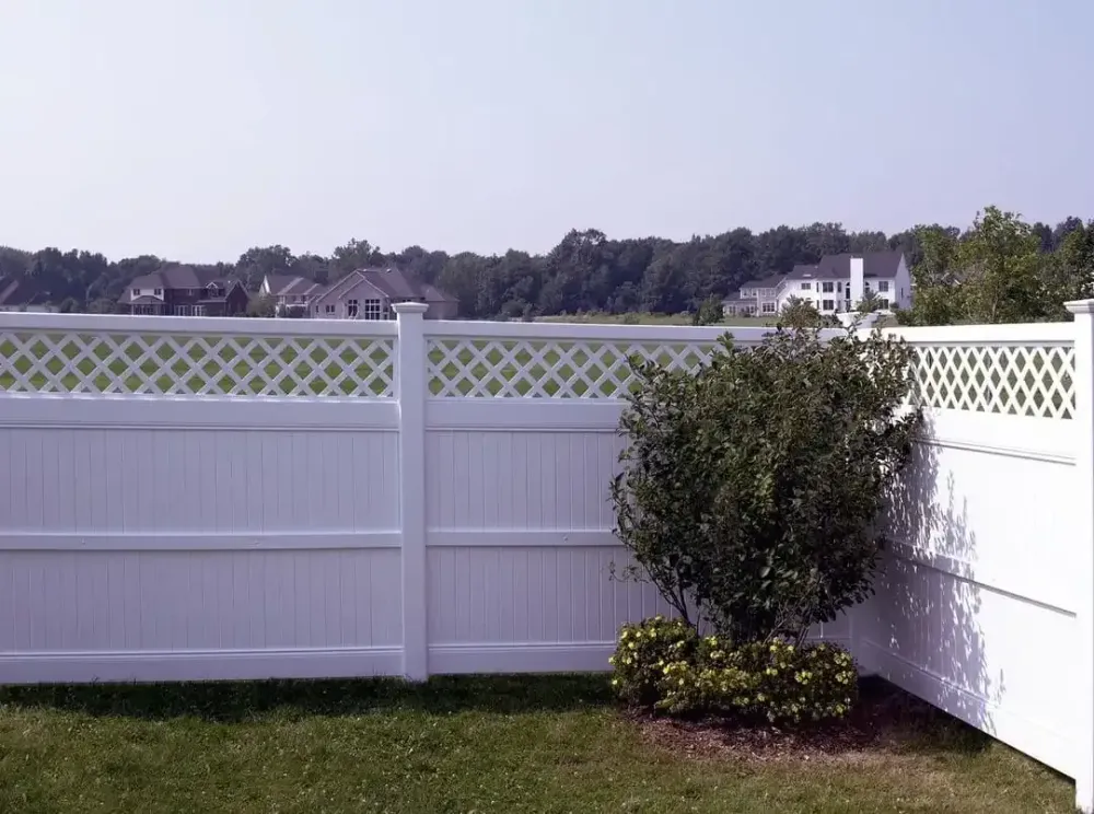 White vinyl fence around a grassy yard with a trimmed bush and water visible in the background