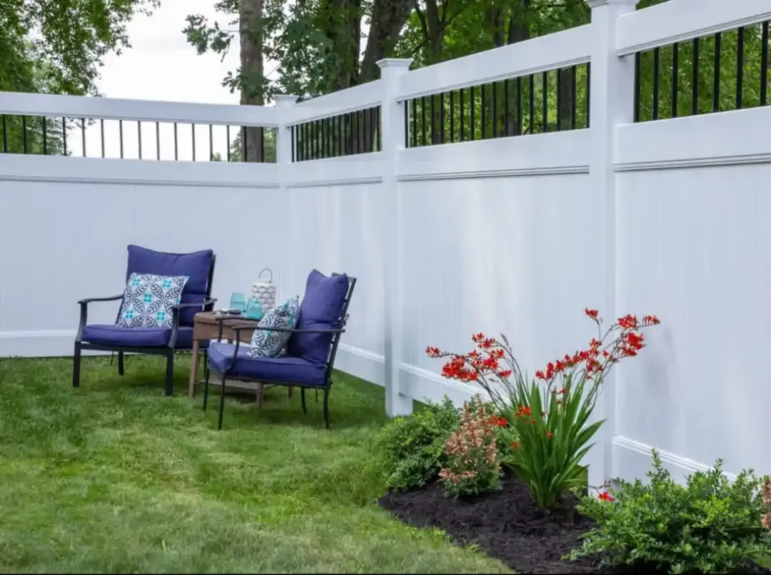 Patio with two blue chairs and a small table beside a white fence and flower bed