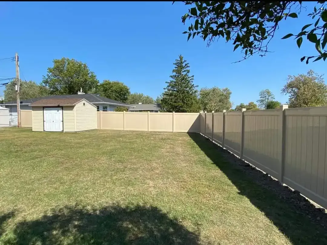Backyard with grass, beige fence, and a small shed under a clear blue sky