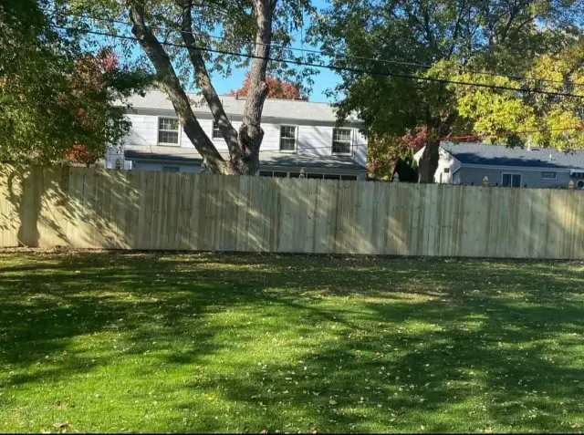 Grassy yard with a wooden fence, trees, and houses in the background on a sunny day