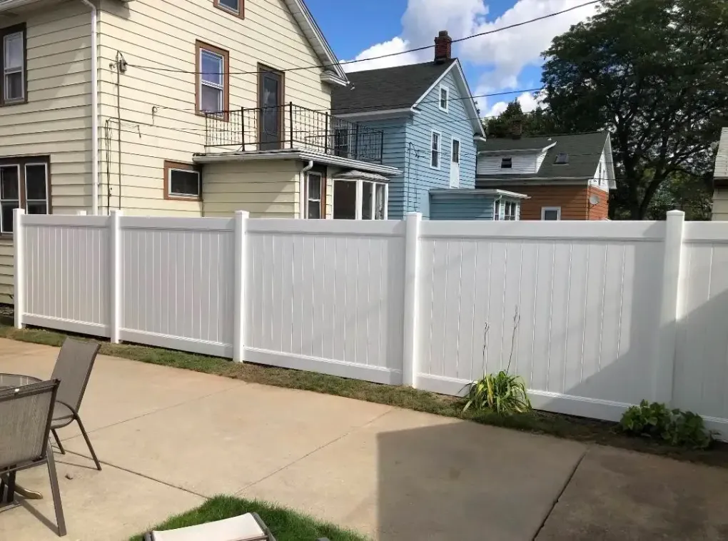 White vinyl privacy fence along a sidewalk beside beige and blue houses under a partly cloudy sky