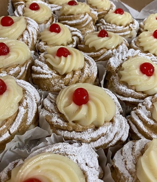 Tray of powdered sugar pastries topped with vanilla cream swirls and red cherries
