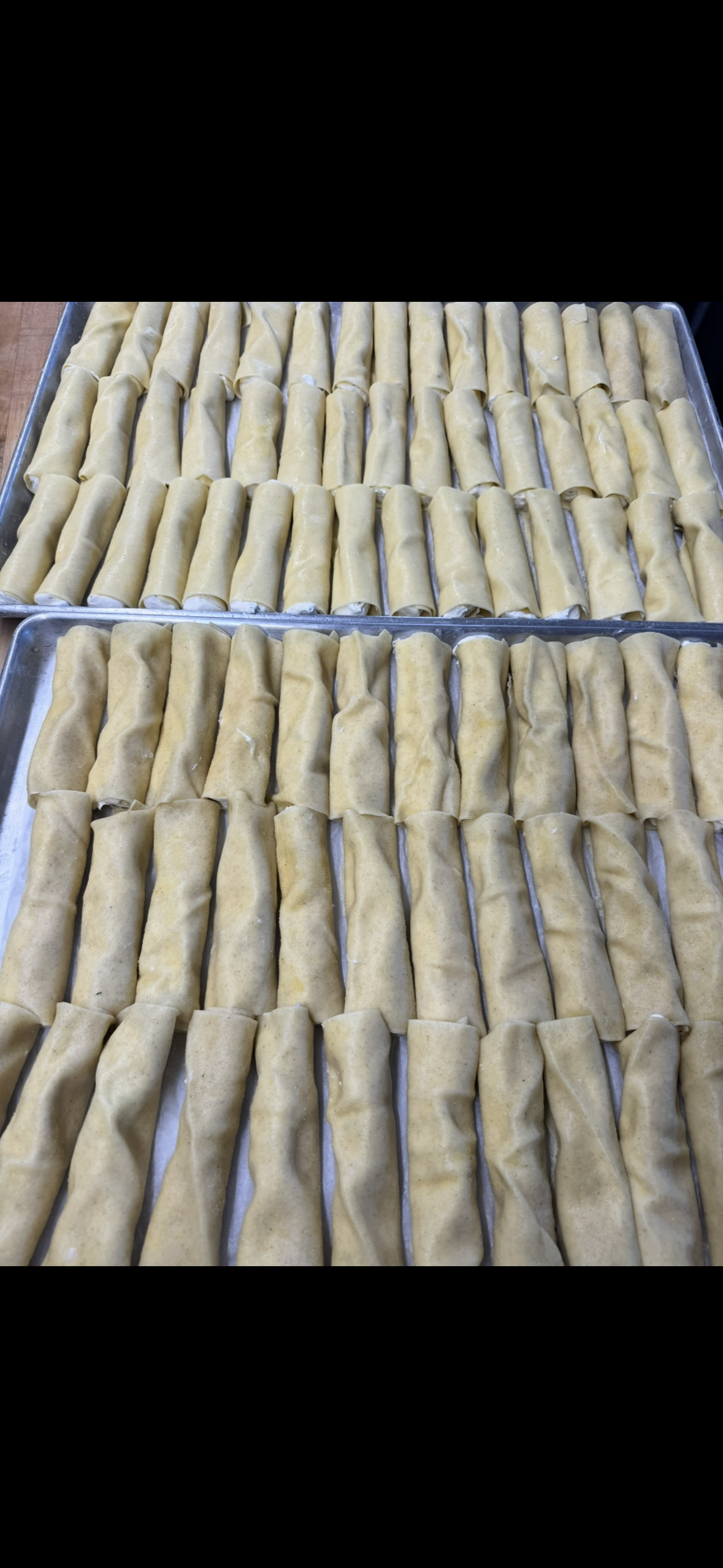 Rows of beige baked rolls arranged on trays, viewed from above