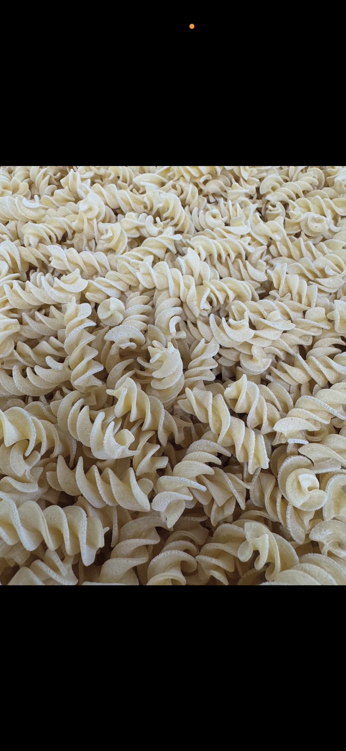 Pile of pale beige dried pasta strips on a dark surface