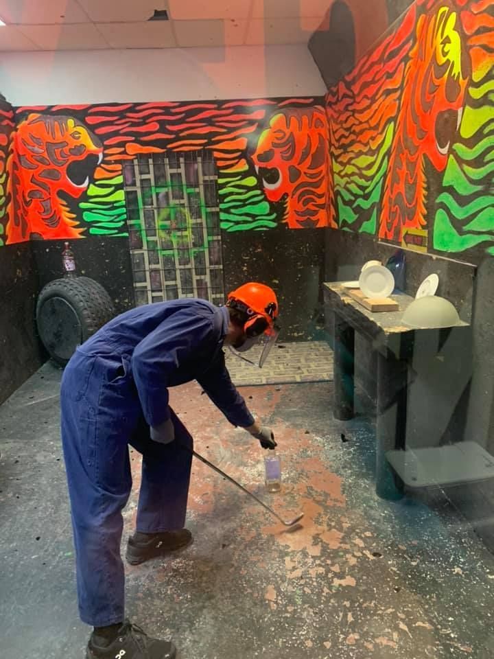 A man in a blue jumpsuit is kneeling down in a room with graffiti on the walls.
