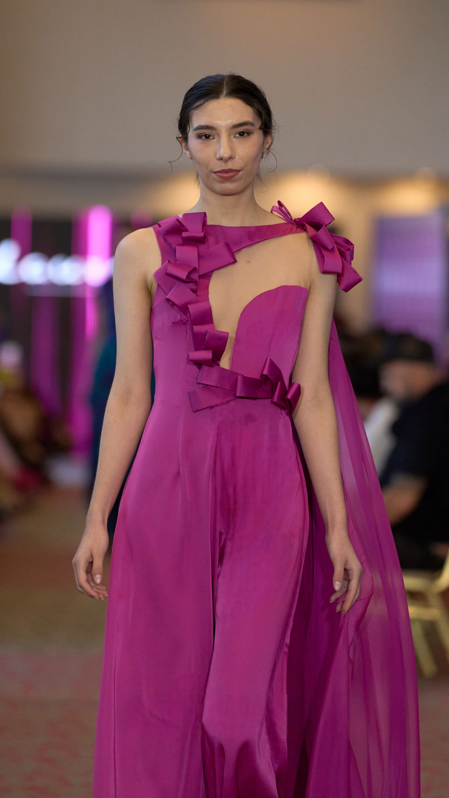 Modelo con vestido magenta caminando hacia la cámara en un desfile de moda.