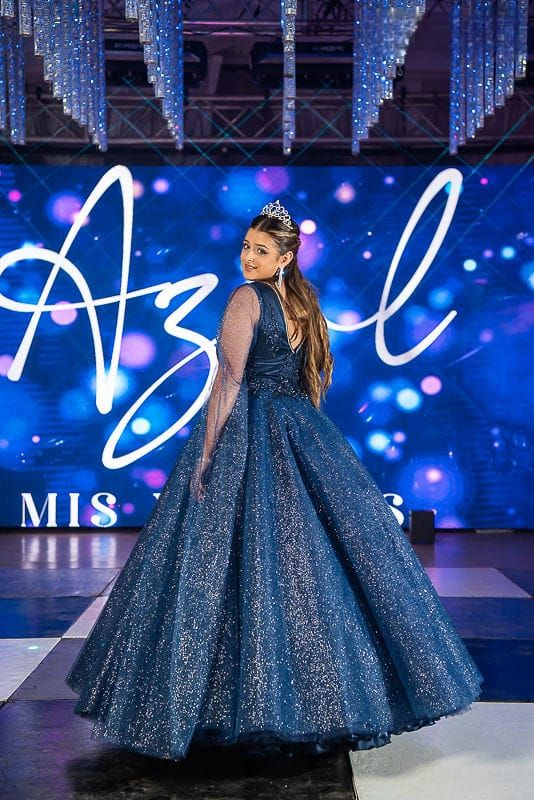 Mujer con un vestido azul brillante de pie sobre un suelo a cuadros en el telón de fondo de un evento formal.