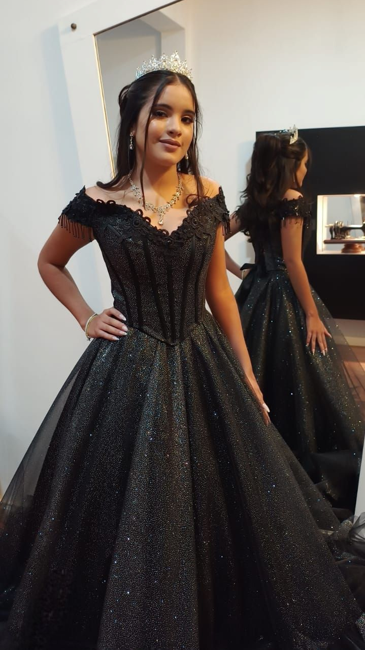 Mujer con un vestido de gala negro brillante posando junto a un espejo en un vestidor.