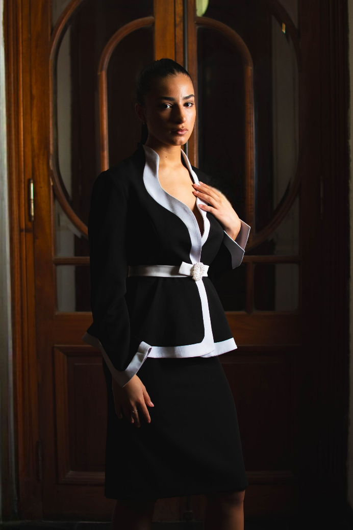 Una mujer con un traje blanco y negro está parada frente a una puerta.
