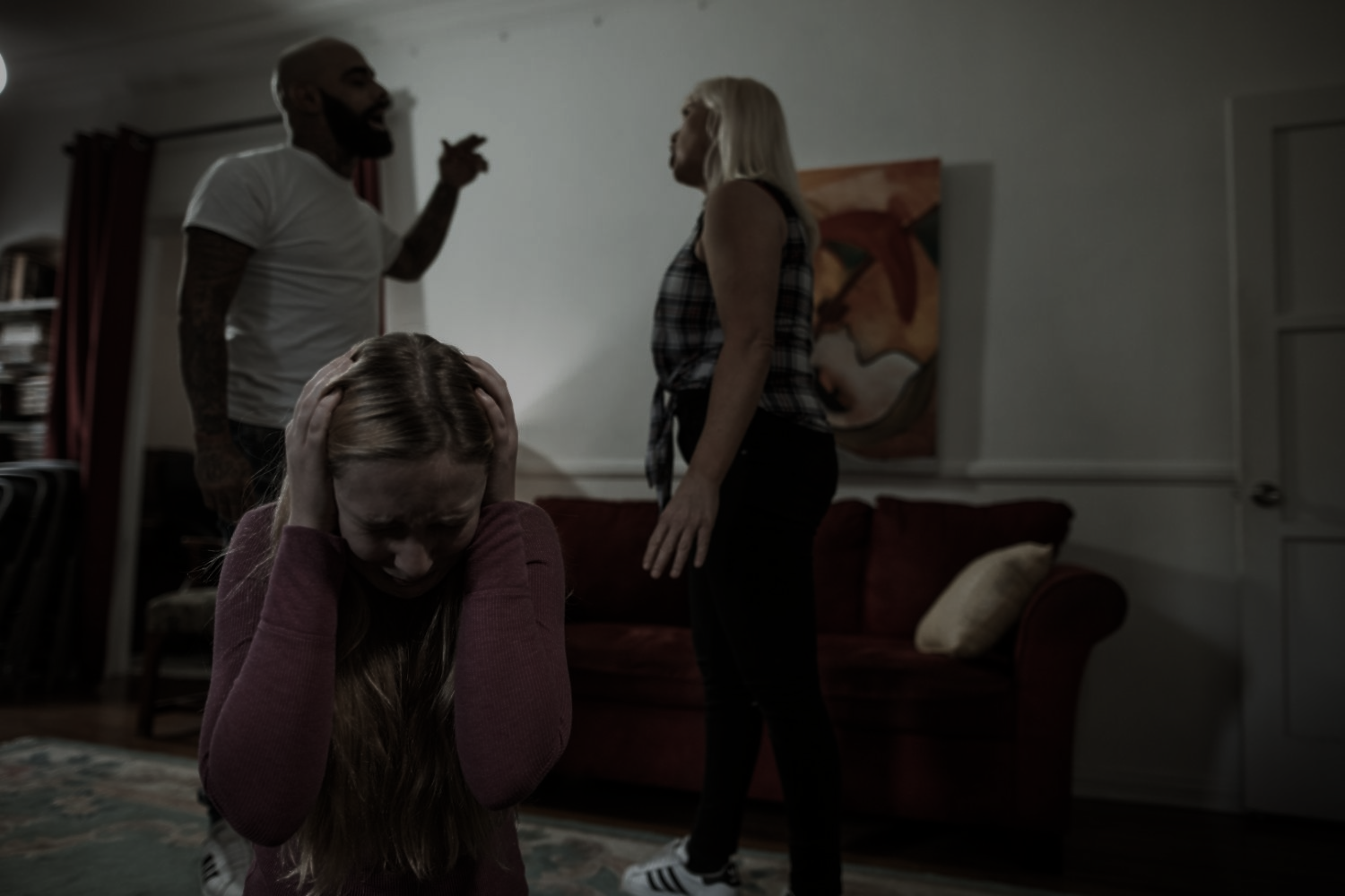 A young girl covers her ears while parents argue in a living room.