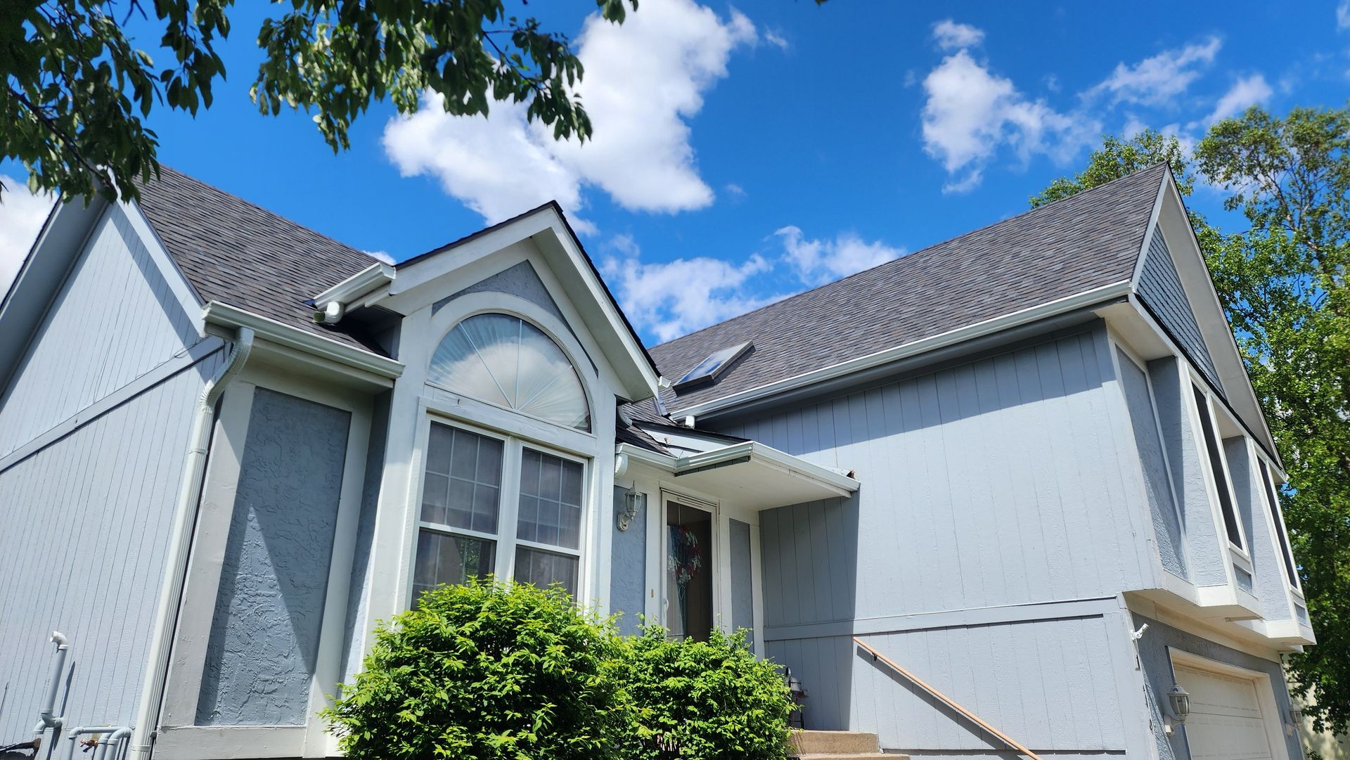 Light blue house with dark gray roof against a blue sky with white clouds.