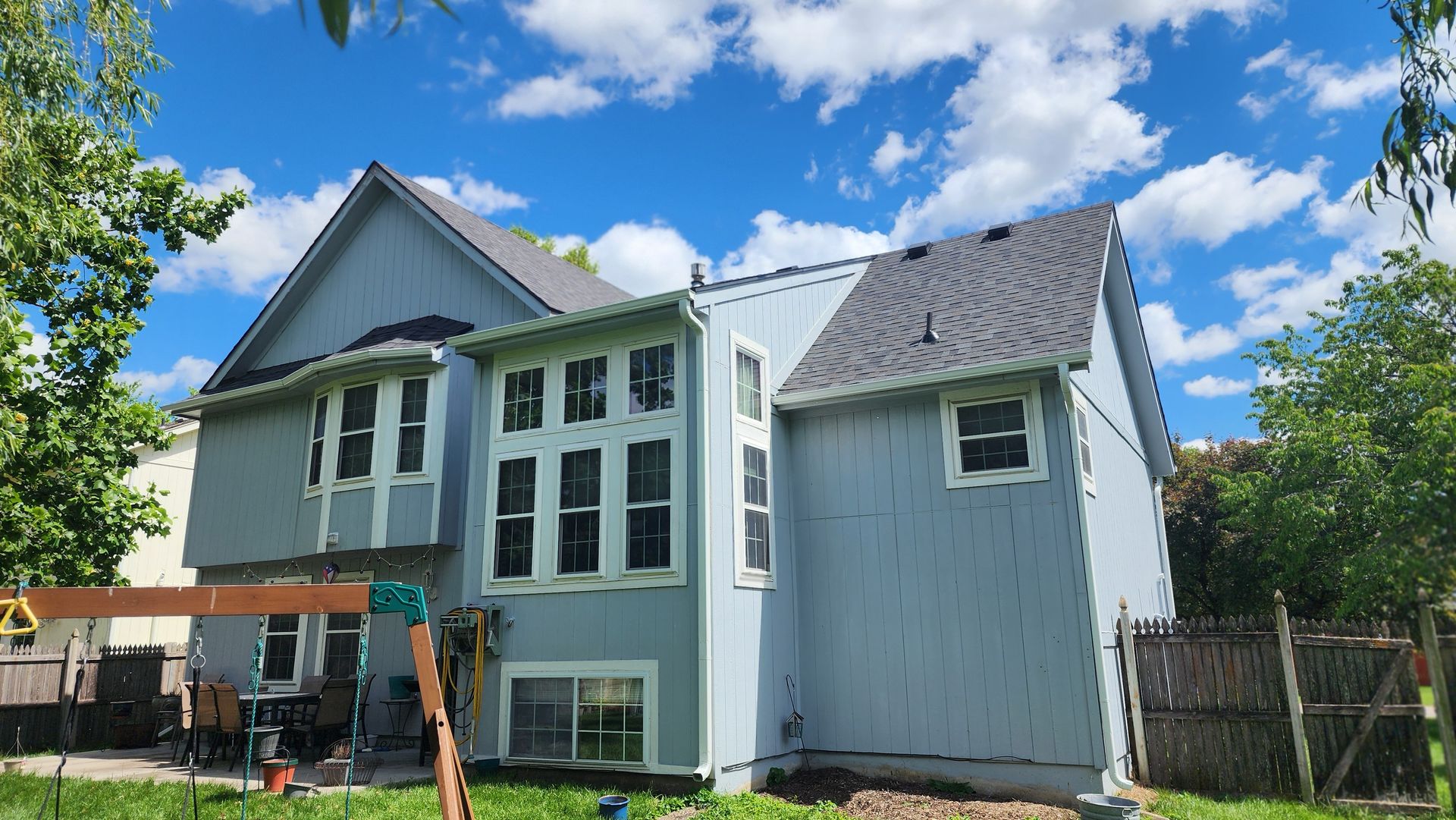 Back of a two-story blue house with multiple windows under a blue sky with clouds.