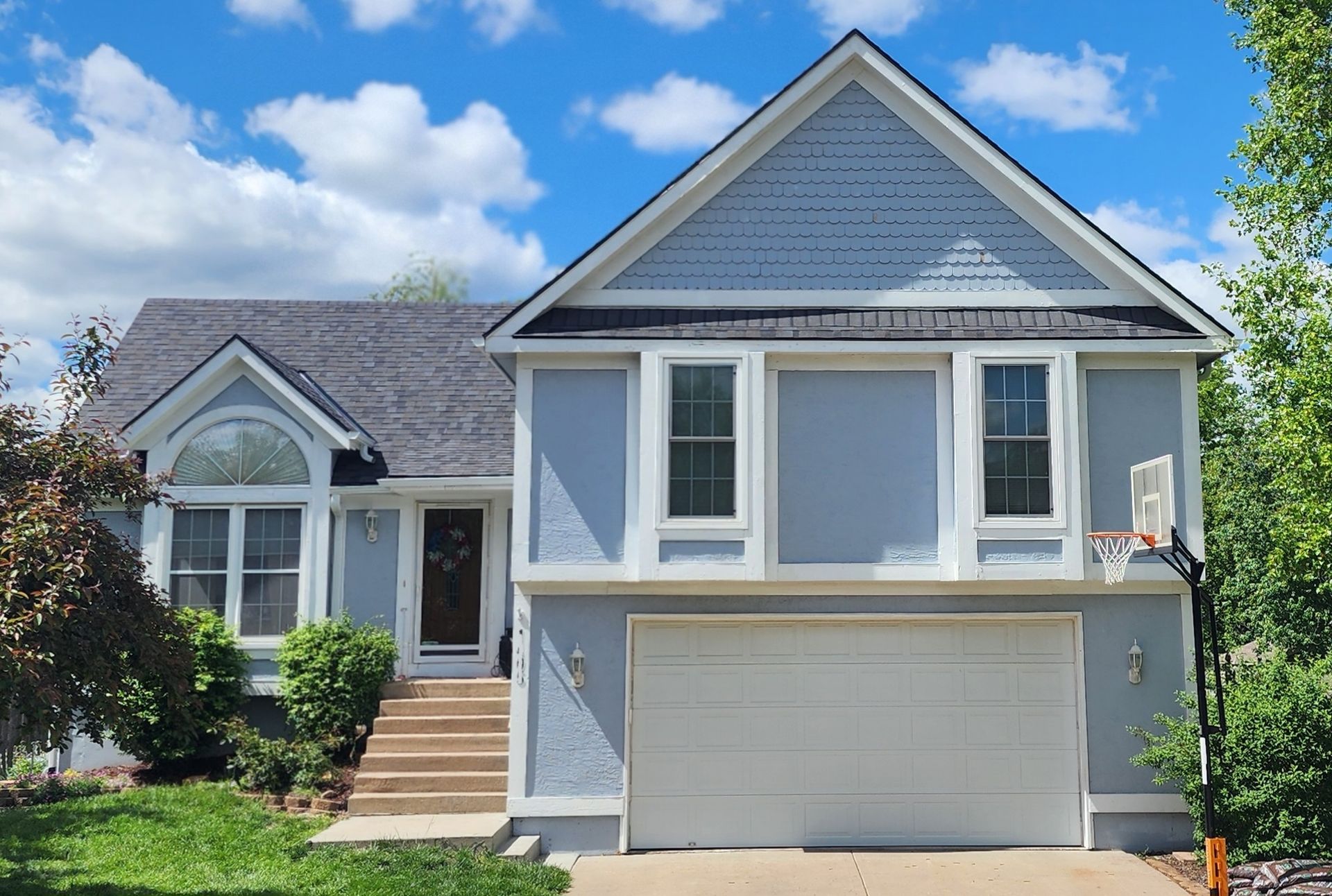 Blue house with white trim, arched window, and gray roof against a cloudy sky.