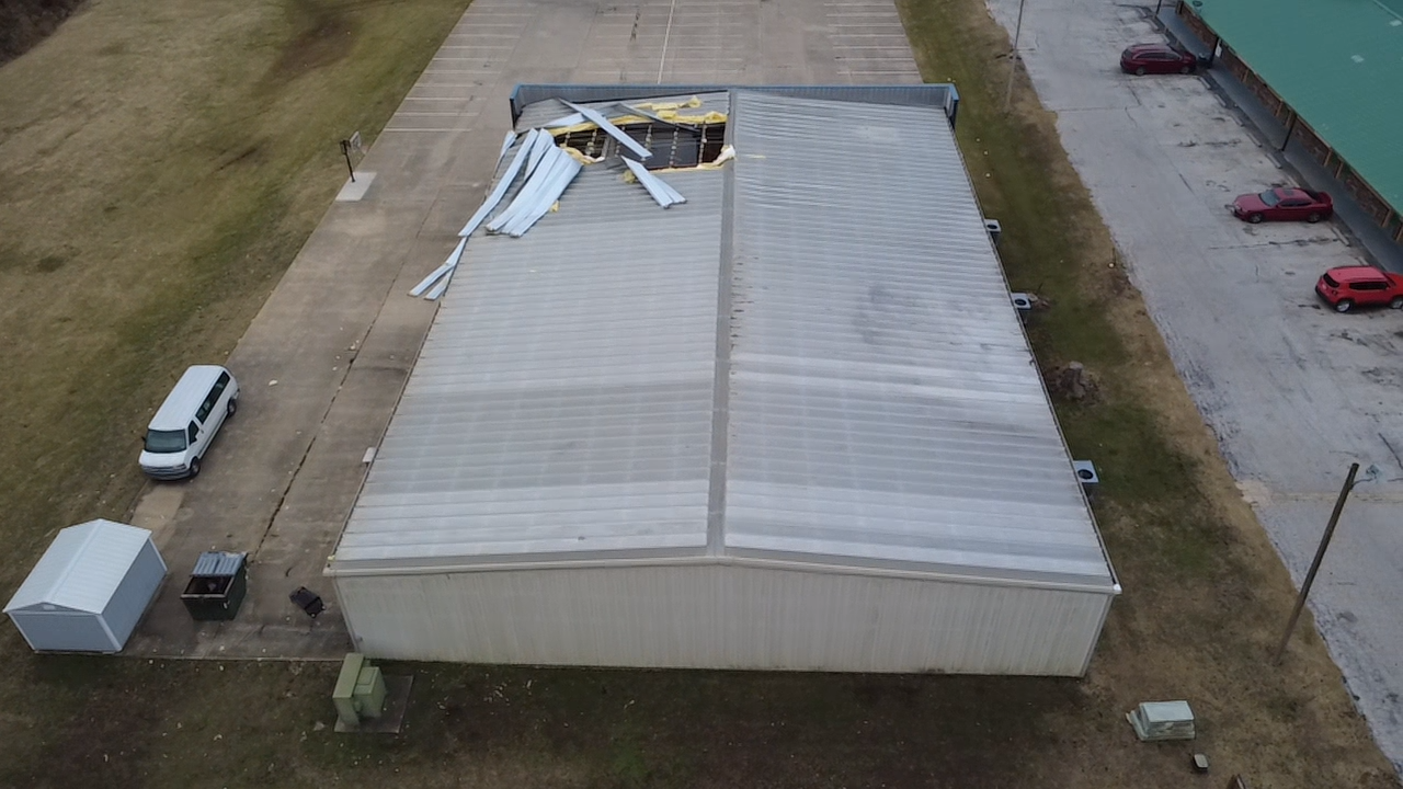 Damaged industrial building with roof partially collapsed; white and gray colors on asphalt.