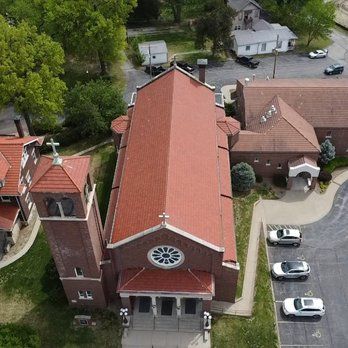 An aerial view of a red-brick church with a tall bell tower and steep, red-tiled roof next to a parking lot.
