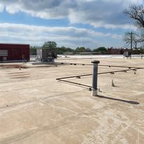 A flat, weathered rooftop under a blue sky with clouds, featuring a pipe, a metal structure, and building sections.