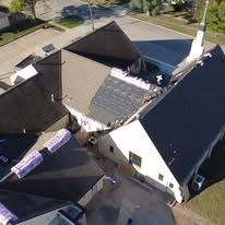 An aerial view of a building roof undergoing construction, featuring partially installed shingles and insulation rolls.