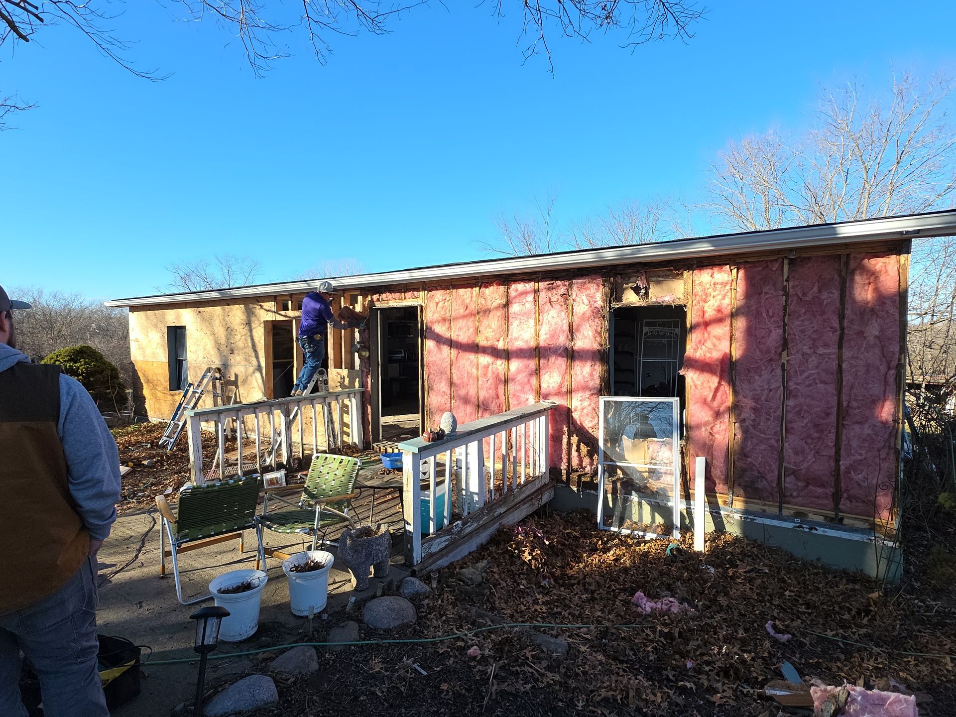 Exterior of a house under construction; insulation visible. A person works in doorway.