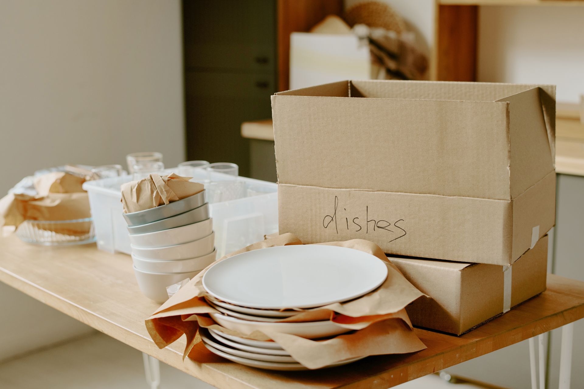 Stacked cardboard boxes and disposable plates on a table, suggesting packing or moving preparations