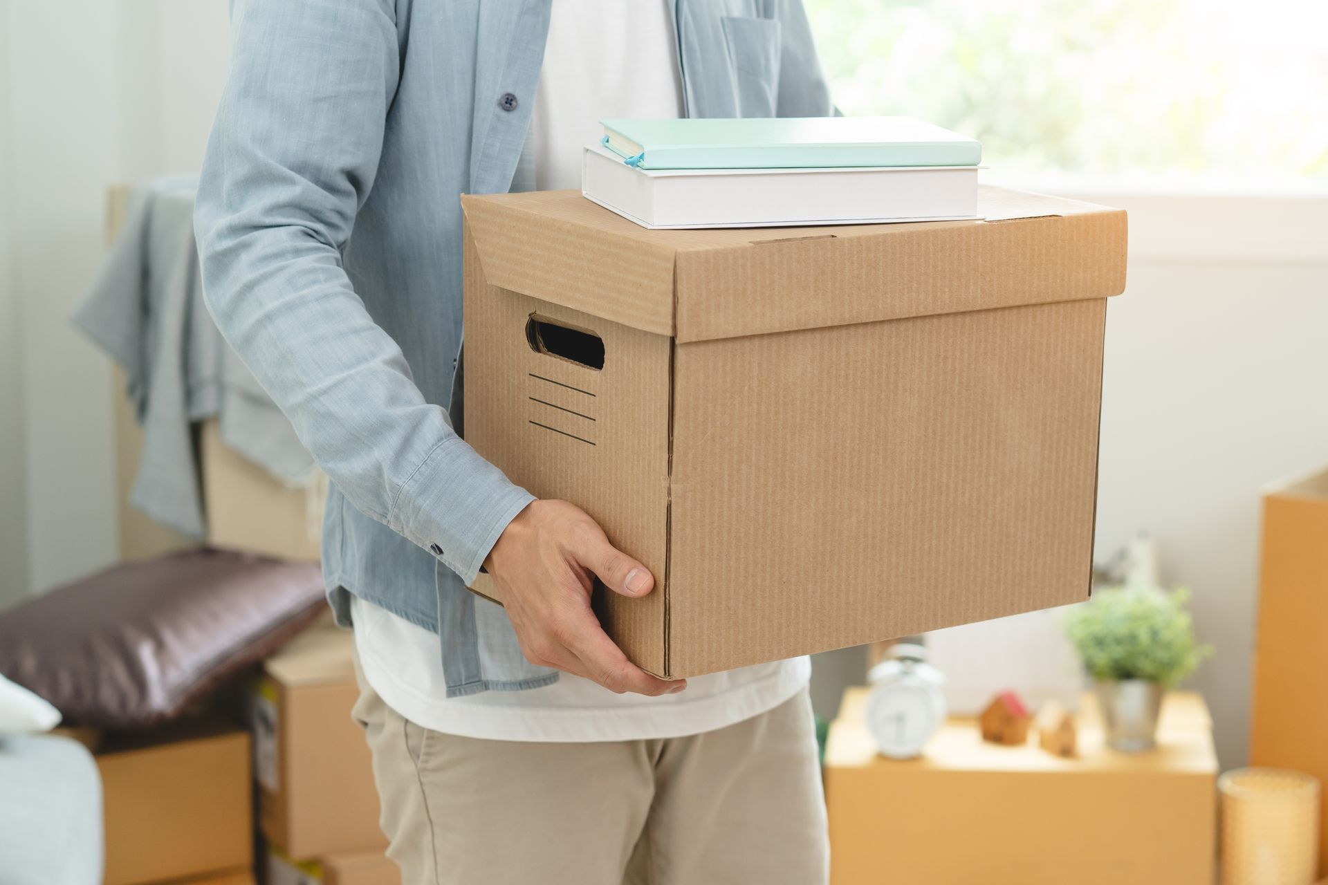 Person holding a cardboard moving box with books in a bright room